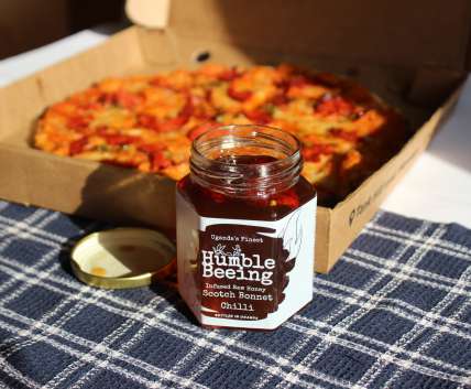 Humble Beeing scotch bonnet chilli infused raw honey jar next to a fresh pizza